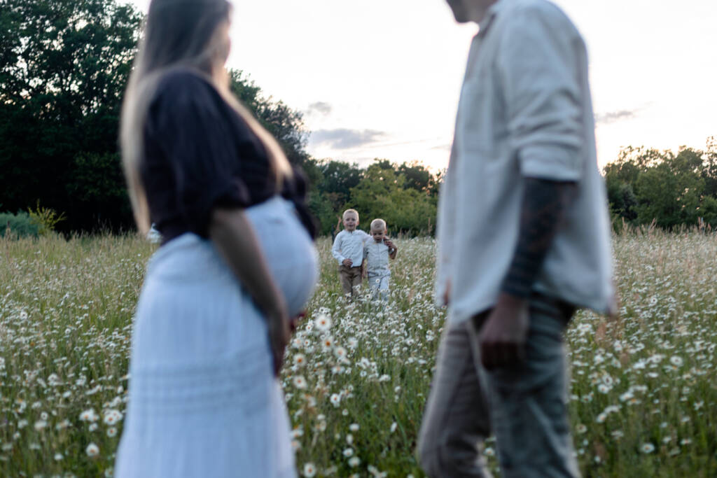 Premier plan flou des parents et du ventre arrondi de maman et les deux grands frères marchant vers eux